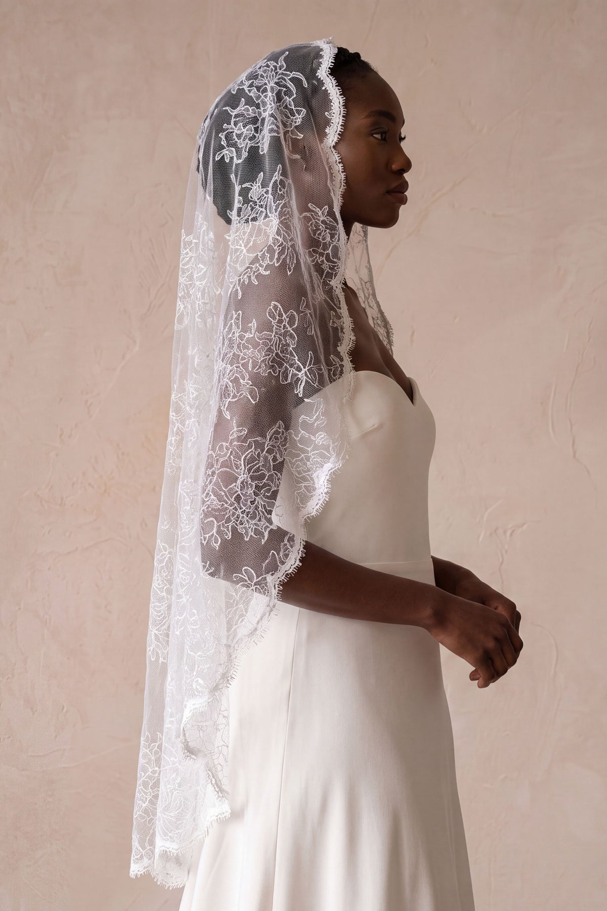 Side profile of a bride wearing a vintage style flat mantilla wedding veil made entirely of sheer floral lace.