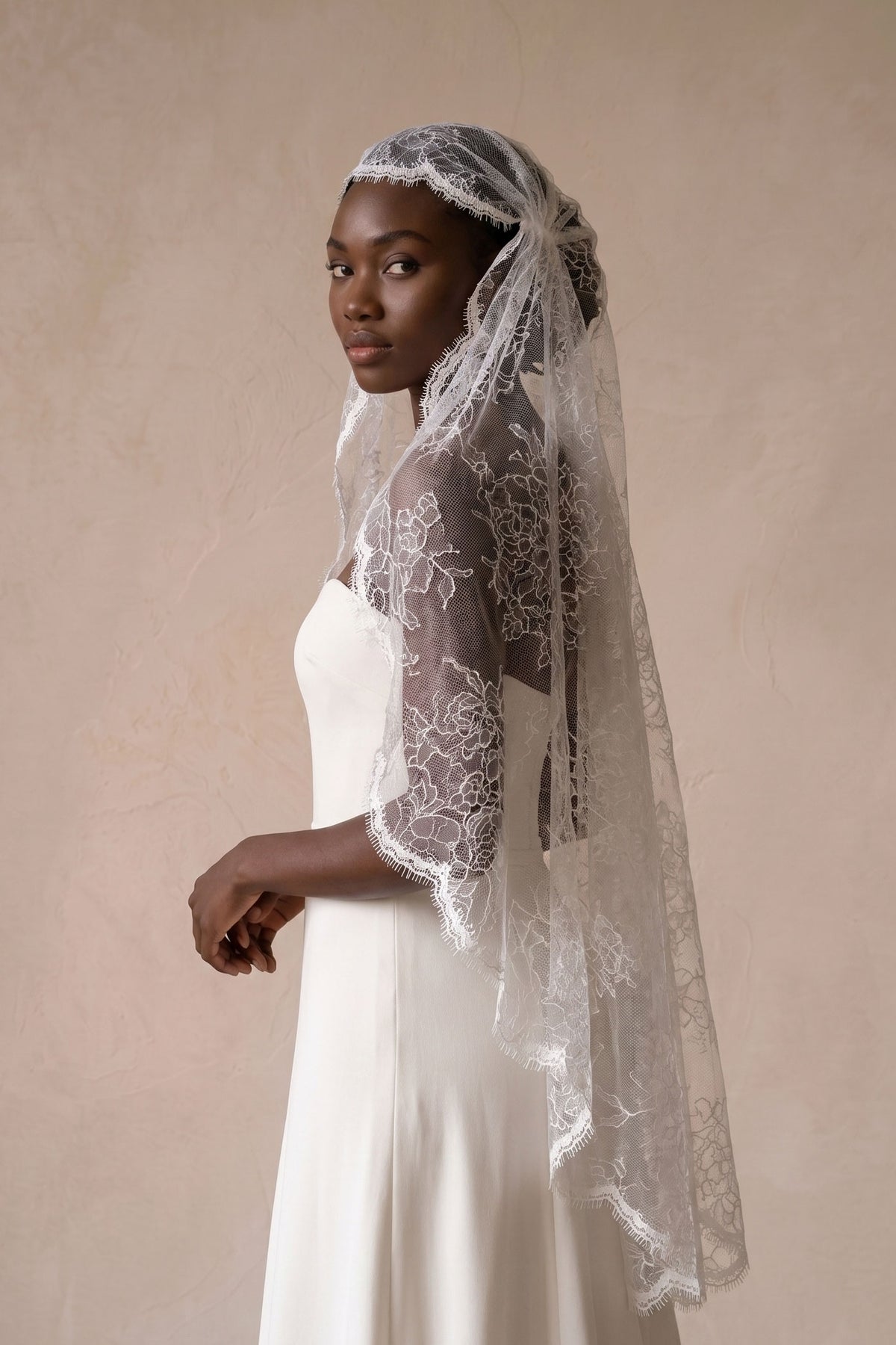 Verona juliet cap wedding veil in all over lace, shown from the side with the scalloped eyelash edge falling past the elbow.