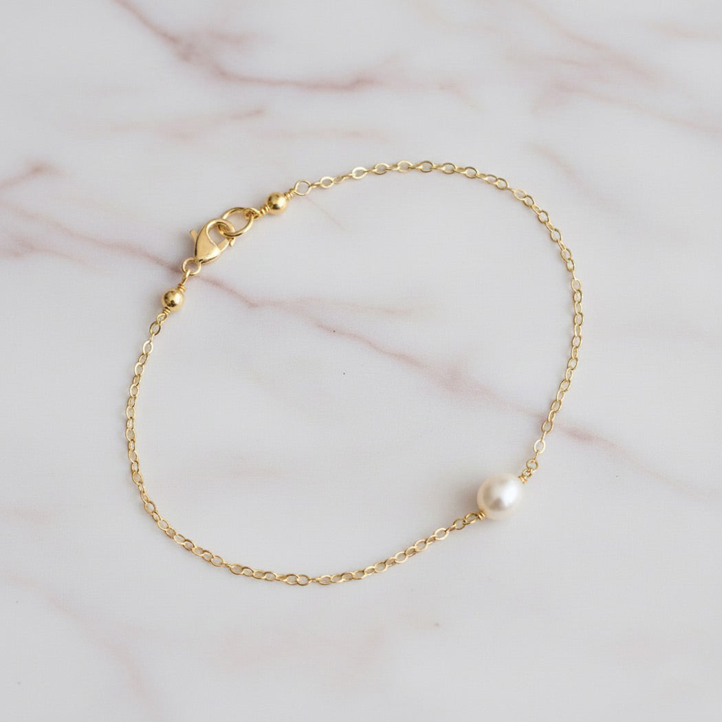 Gold bracelet with a pearl on a marble surface