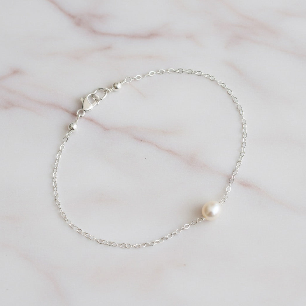Silver chain bracelet with a single pearl on a marble surface