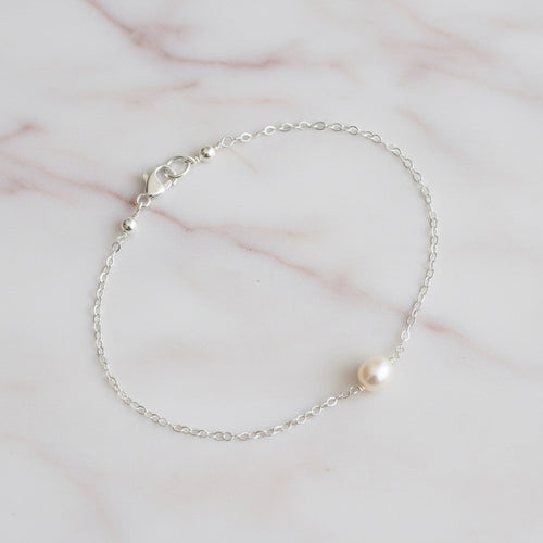 Silver chain bracelet with a single pearl on a marble surface