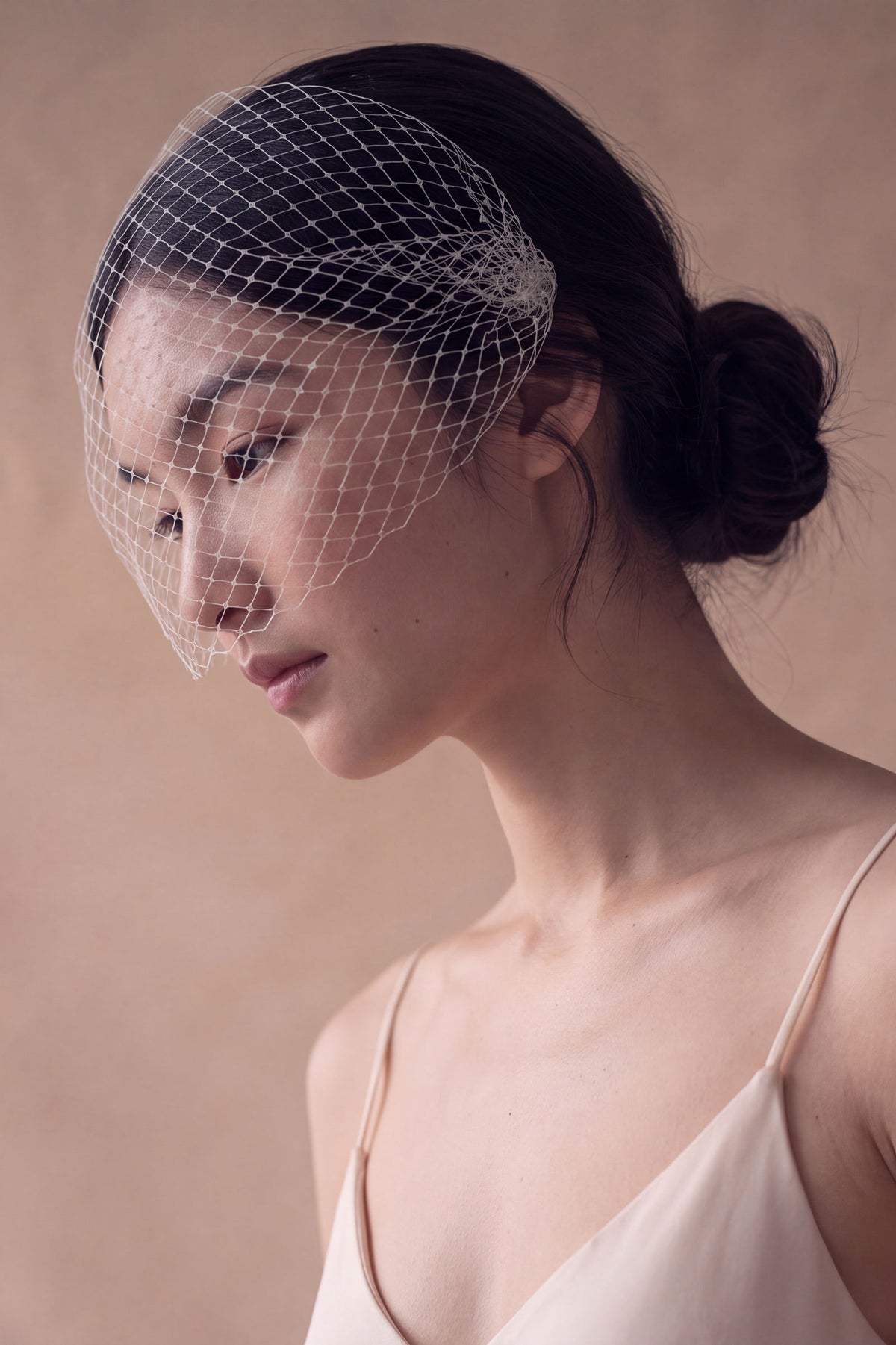 Iris ivory Russian net birdcage veil worn over the eyes with a low bun, handmade by Britten Weddings