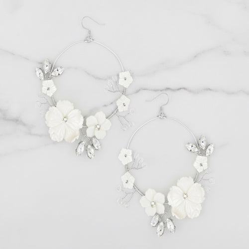 Pair of white floral hoop earrings on a marble surface. Silver