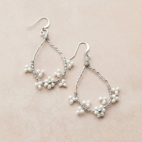 Silver hoop earrings with pearl-like beads on a beige background