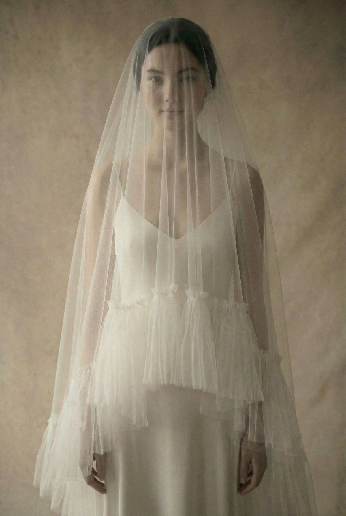 Close-up detail of a traditional tulle blusher veil worn over the bride's face. The sheer fabric provides a soft, romantic look, while the wide ruffle edge creates a unique textured detail across the bodice.